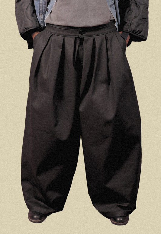 Man wearing coated black denim double waistband wide-leg trousers on a beige background