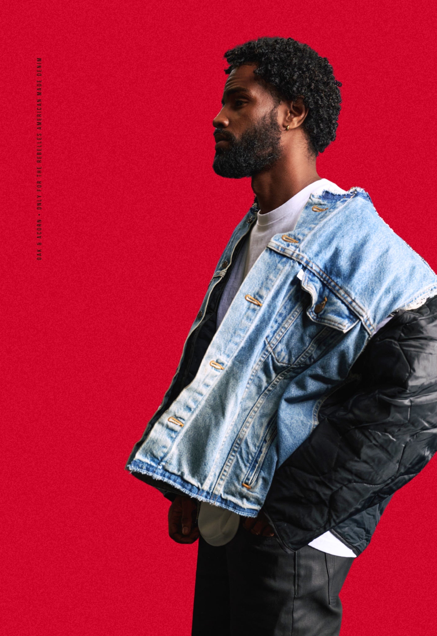 Man wearing a black quilted repurposed denim jacket over a heavyweight white t-shirt on a red background